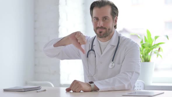 Young Doctor Showing Thumbs Down While Sitting in Clinic
