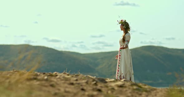 Beautiful Woman in a Folk Dress with Embroidery and a Floral Wreath on Her Head Sings in the