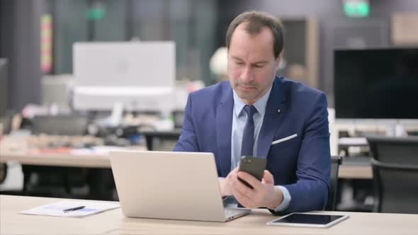 Businessman Using Smartphone While Using Laptop in Office