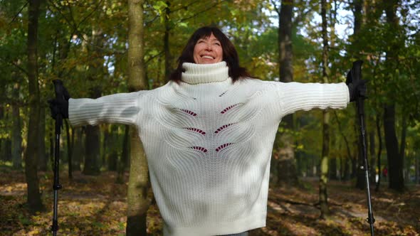 Front View of Happy Smiling Mature Woman Stretching Hands Looking Up Standing in Autumn Park at