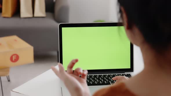 Young Asian woman using laptop computer at home with green blank monitor screen.