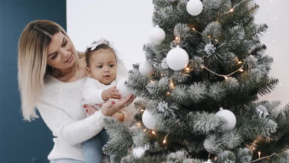 Mom and Baby Girl Sitting and Decorating Christmas Tree Together