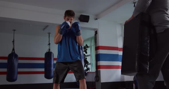 Caucasian man training with coach in boxing gym