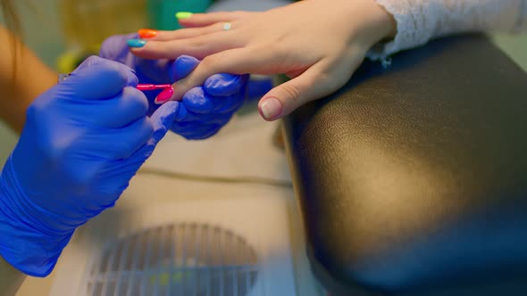 Unrecognizable Person in Gloves Paints Nails of Young Woman in Salon