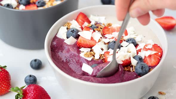 Eating with Spoon Berry Smoothie Bowl with Granola, Strawberries, Blueberries and Coconut. 