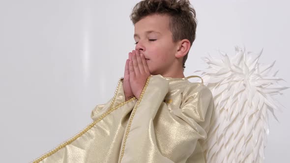 Little Boy Who Sincerely Prays with Folded Arms on a White Background