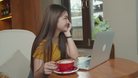 Young Asian Girl Looking Outside at a Coffee Shop with a Laptop