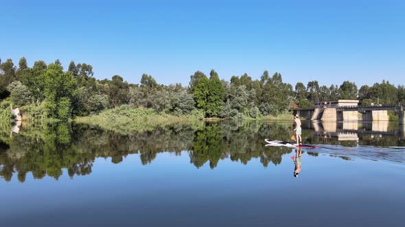 aerial footage of a man SUP paddling at a dam