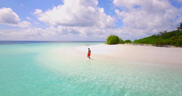 Aerial view of a man walking on the beach around a tiny deserted tropical island