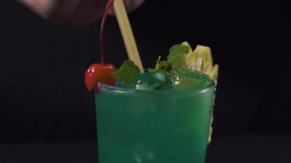 Bartender's Hand Putting a Drinking Straw in a Glass of Green Tropical Cocktail.