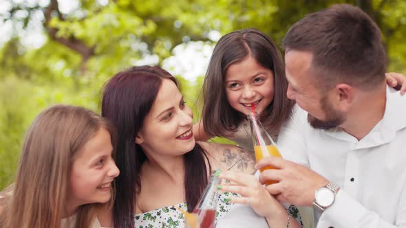 Smiling Father Mother and Two Cute Daughters Drinking Fresh Juice at Green