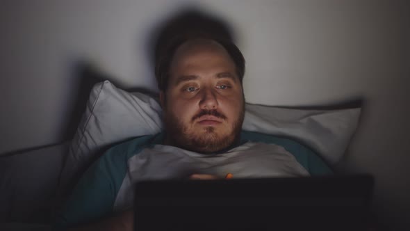 Fat Guy on Diet Watching Video on Laptop at Home in Bed at Night Eating Carrot Sticks