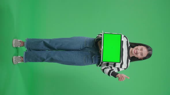 Asian Woman Showing Thumbs Up Gesture While Holding Green Screen Computer In The Green Screen Studio