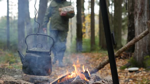 Camping Kettle over Burning Fire and a Hiker with Firewood