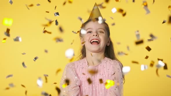 Happy Girl Throwing Confetti. Excited Laughing Kid in Pink Dress and Party Cap.