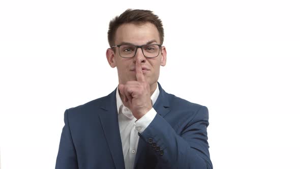 Attractive Businessman in Blue Suit and Glasses Shushing at Loud Person Shaking Finger to Scold