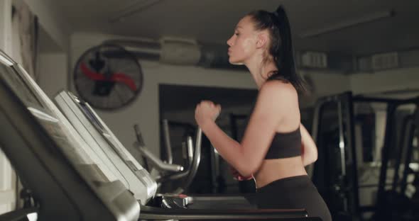 Side View of Concentrated Girl with Tied Hair Jogging on a Treadmill in Gym