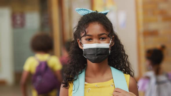 Portrait of mixed race schoolgirl wearing face mask, standing in corridor looking at camera