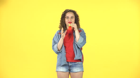 Curly Girl Inflates a Bright Red Ball on Yellow Background at Studio