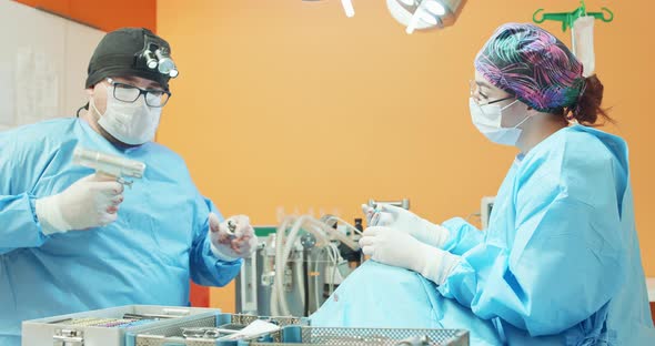 Male Veterinarian in Glasses White Gloves Cap and in Surgical Outfit Disassembles the Drill