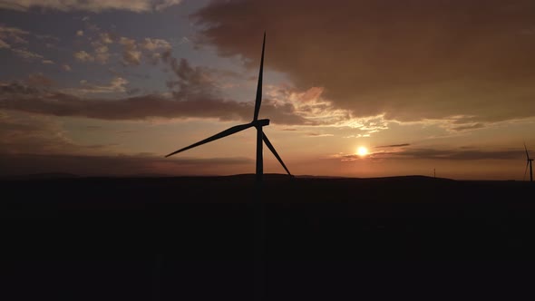 Silhouette of windmill turbine in field at sunset sky. Rotating wind generator