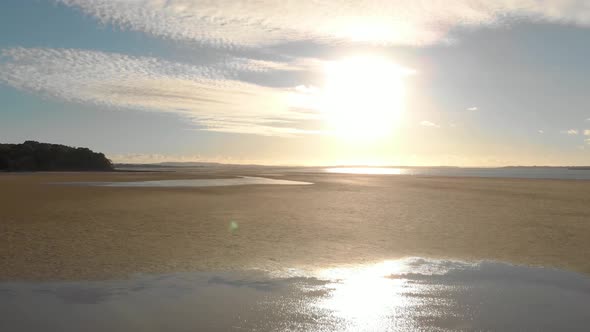 Low flying aerial shot to rising up of the sunrise over sand and water at Andersons inlet in Victori