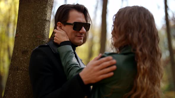 a Blonde in a Green Jacket Strokes a Man's Hair and Takes Off His Sunglasses in an Autumn Park on a