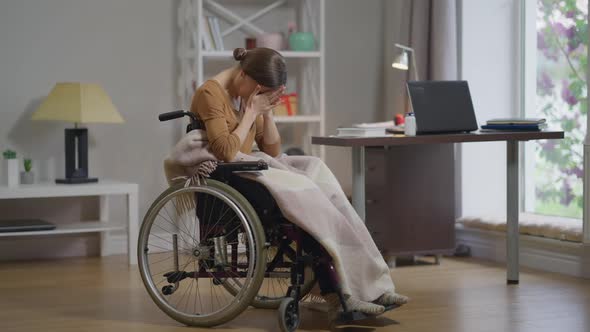 Overwhelmed Young Disabled Woman in Wheelchair Closing Face Crying Alone at Home