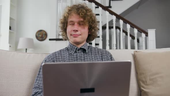 Young Guy Sitting on the Comfortable Sofa at Home and Working on Laptop