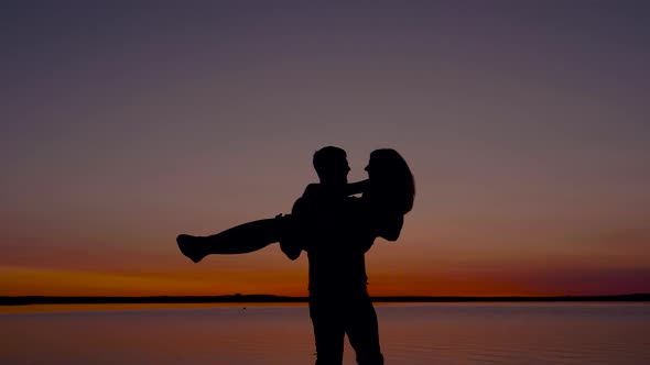 Silhouette Of A Man Holding A Woman And Circling Her At Sunset By The Sea