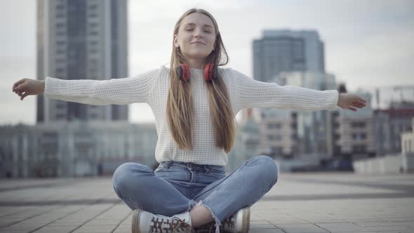 Relaxed Caucasian Woman Sitting in Lotus Pose on Overcast City Square. Portrait of Calm Smiling