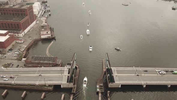 Aerial tilp up shot of a line of boats sailing under a drawbridge in the Mystic River.