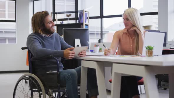 Disabled caucasian businessman sitting on wheelchair using digital tablet talking to coworker in off