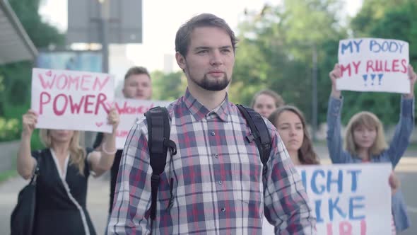 Young Confident Caucasian Man Raising No Sexism Banner with Crowd of Activists Shouting at the