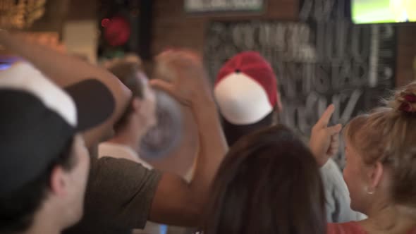 Football fans cheering while watching televised match at sports bar