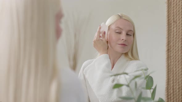 Pretty Female Doing Facial Massage in Bright Bathroom