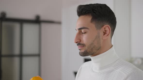 Joyful Young Middle Eastern Man with Brown Eyes Smelling Vitamin Orange Looking at Camera Smiling