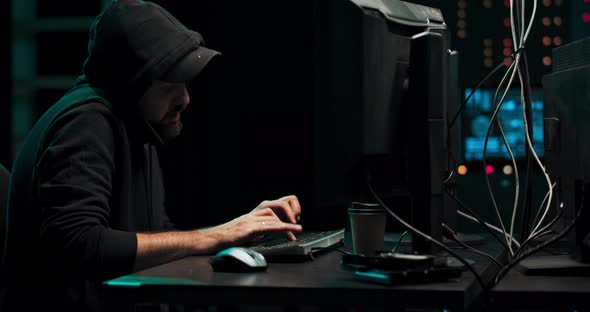 Concentrated Hacker in Hooded Sweatshirt and Peaked Cap Breaks Into Corporate Servers From His