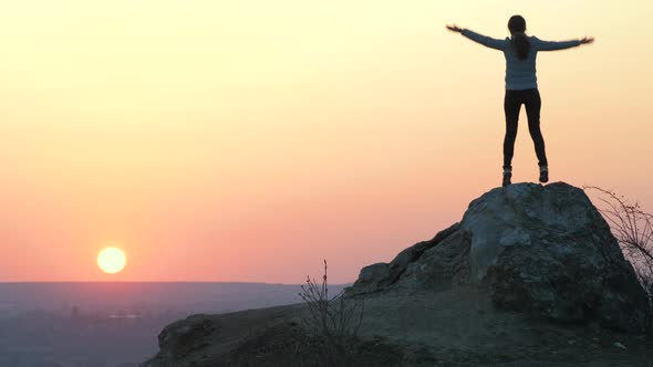 Silhouette of a Woman Hiker Climbing Alone on Big Stone at Sunset in Mountains