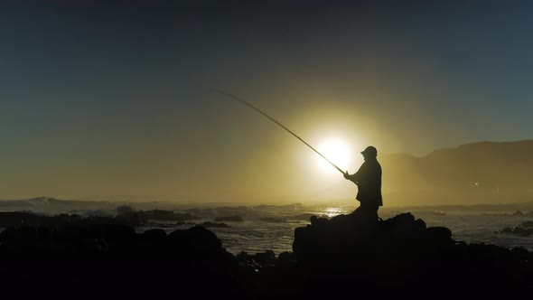 Fisherman on rocks appears to be reeling in a fish, but it's something totally different.