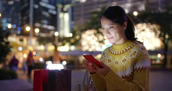 Woman use of mobile phone use of mobile phone with shopping bag in city at night