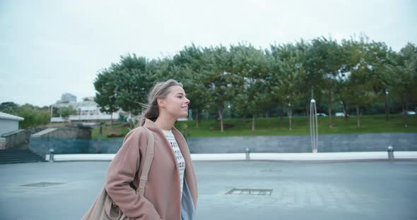 Woman Walks Smiling Along Windy Deserted Street at Twilight