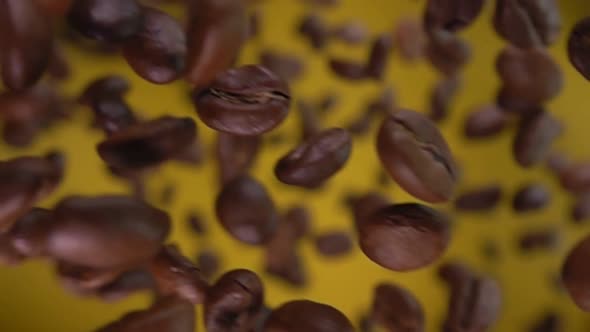 Close-up of Roasted Coffee Beans Flying Diagonally on the Yellow Background