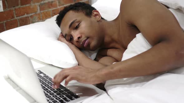 African Man Typing Email on Laptop Lying in Bed for Rest