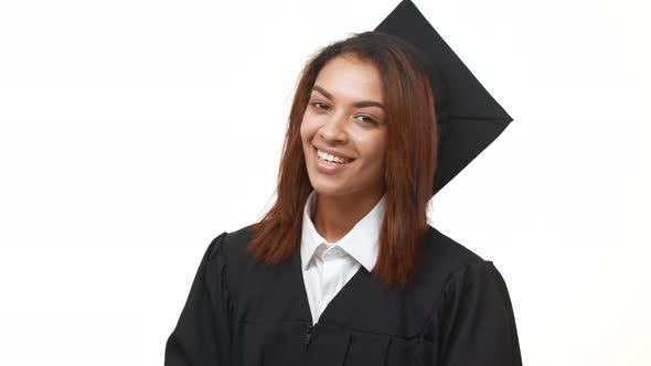 Young Happy African American Female Graduate Student Standing Over White Background in Black Robe