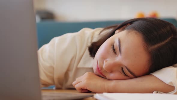 Bored Asian woman going to sleep on the table after working on laptop