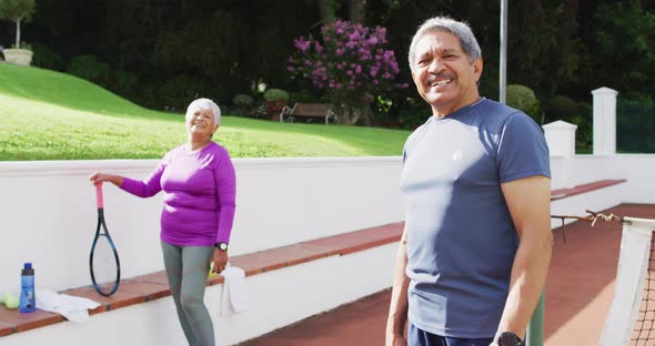 Video of happy biracial senior couple looking at camera on tennis court