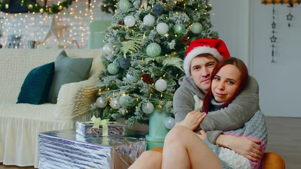 Man and Woman Hugging Tenderly Sitting on Floor Near Christmas Tree in Living Room