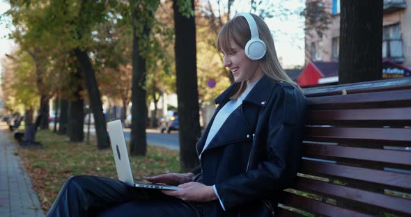 Happy Young Woman with Headphones Using a Laptop in the Park