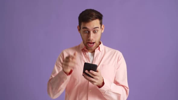 Studio Portrait of Surprised Excited Young Man Screaming During Using Mobile Cell Phone Just Found